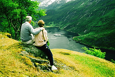 Rear view of two people sitting near a river, Geiranger Fjord, Norway