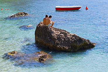 Tourists sitting on a rock, Capri, Campania, Italy