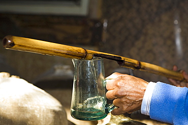 Close-up of a person's hand pouring pisco in a glass from a bamboo stick, Ica, Ica Region, Peru