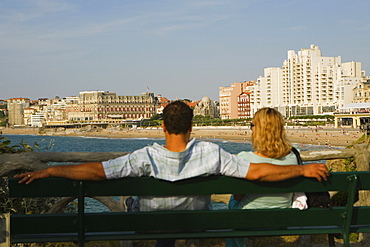 Rear view of a couple sitting on a bench, Grande Plage, Hotel du Palais, Biarritz, France