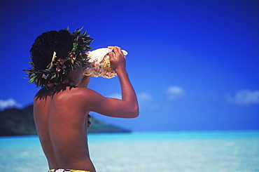 Rear view of a child blowing a conch shell on the beach, Hawaii, USA