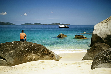 Rear view of a topless man resting on a rock at a seashore, Virgin Gorda, Virgin Islands