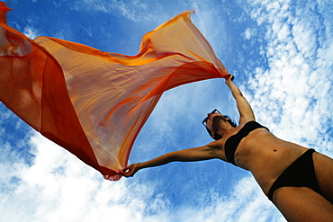 Woman holding a orange colored fabric in the tropical breeze on the island of Barbados, Caribbean