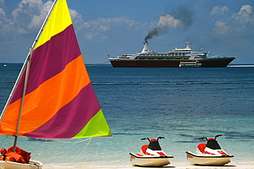 Side view of a boat with a colorful sail with the Starship Majestic Cruise Ship in the background, Treasure Island, Bahamas