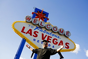 Low angle view of a young man standing in font of a Las Vegas sign board, Las Vegas, Nevada, USA