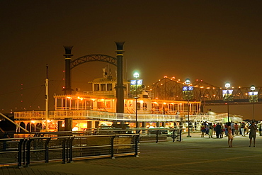 Group of people walking in front of an illuminated paddle steamer moored at a harbor, New Orleans, Louisiana, USA