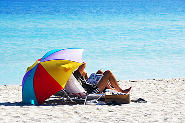 Two people under a beach umbrella, Miami, Florida, USA