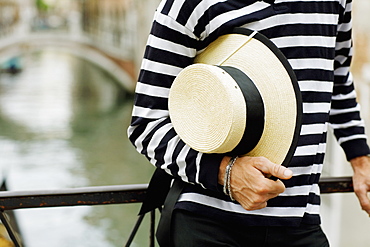 Mid section view of a gondolier standing and holding a hat, Venice, Veneto, Italy