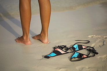 Low section view of a woman standing on the beach near a bikini