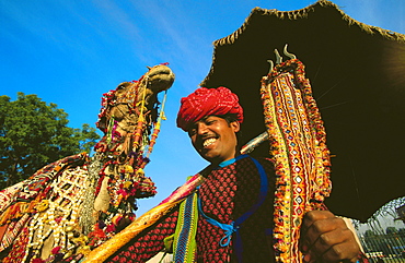 Young man holding a trident and standing near a camel, Jaipur, Rajasthan, India