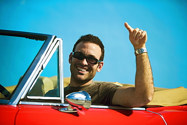 Close-up of a mid adult man sitting in a convertible car pointing forward, Miami, Florida, USA