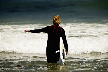 Rear view of a man walking into the sea with a surfboard