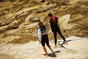 Rear view of two surfers walking on the beach, La Jolla Reefs, San Diego, California, USA