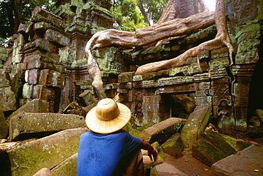 Rear view of a man sitting on a stone in front of a temple, Ta Prohm Temple, Angkor, Siem Reap, Cambodia