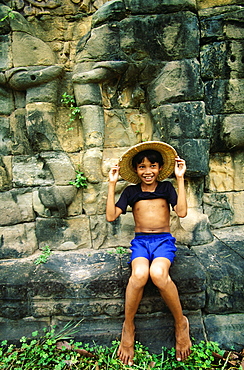 Boy sitting on a ledge and smiling, Angkor Thom, Angkor, Siem Reap, Cambodia