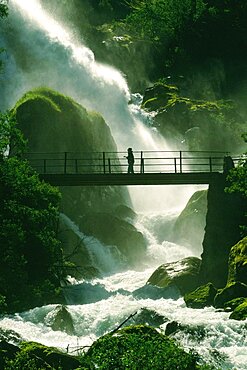 Person crossing a waterfall on a footbridge, Olden, Norway