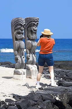 Rear view of a woman taking a photograph of tikies on the coast, Puuhonua O Honaunau National Historical Park, Kona Coast, Big Island, Hawaii Islands, USA