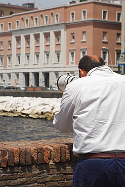 Rear view of a man with a hand-held telescope, Via Partenope, Bay of Naples, Naples, Naples Province, Campania, Italy