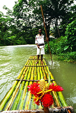 A man is standing on a bamboo raft floating down the Martha Brae River, Jamaica