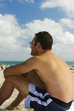 Side profile of a mid adult man sitting on the beach