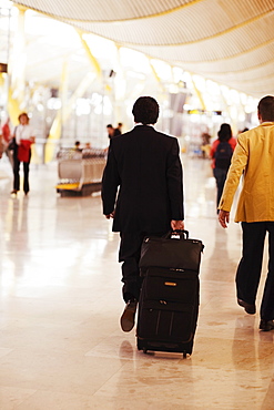 Rear view of a man walking and pulling luggage at an airport, Madrid, Spain