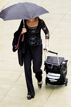 High angle view of a woman walking with an umbrella and suitcase