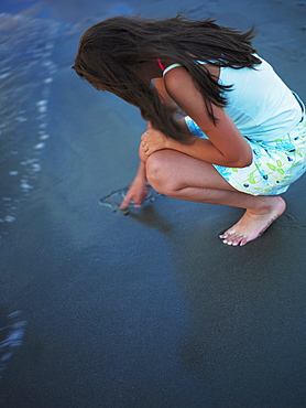 High angle view of a teenage girl drawing in the sand with her finger