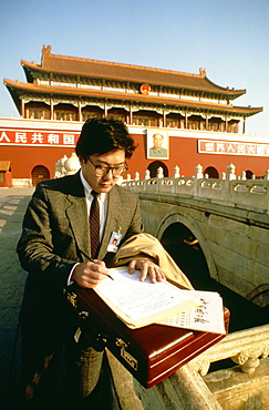 Businessman standing in front of a palace and writing with a pen on a sheet of paper, Tiananmen Gate Of Heavenly Peace, Tiananmen Square, Beijing, China