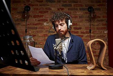 Man wearing headphones reading, speaking into microphone