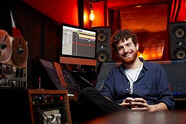 Portrait of man smiling, sitting in music studio holding cup of coffee