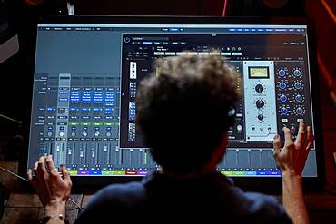 Man working in music studio using large computer screen shot from behind