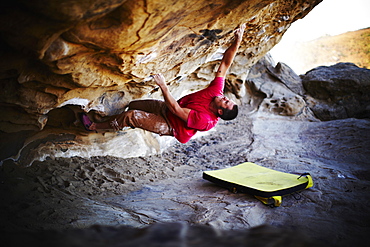 A man free climbing on the overhang of a rock face, with minimum equipment, USA