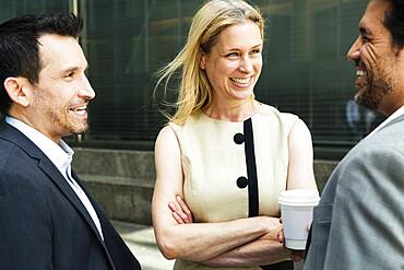 Businesswoman and two businessman standing outdoors, chatting and smiling, New York, United States of America