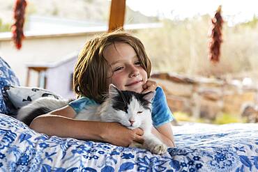 Young boy lying on outdoor bed stroking a pet cat