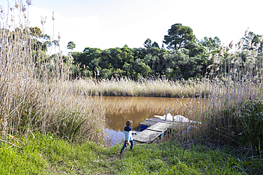 Young boy playing near a lagoon on the Klein River estuary, boat moored at a dock