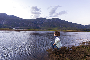 A boy exploring the shore of a lagoon in the shadow of the Kleinriver mountain range