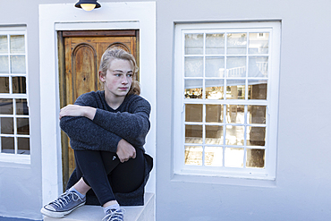 Teenage girl sitting cross legged on a low wall outside a house