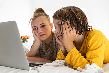 Young boy and teenage sister sharing a laptop, watching in a bedroom