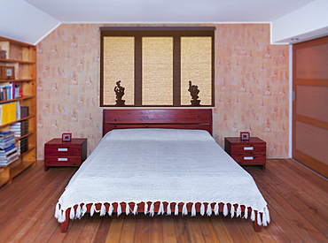 Bedroom interior with large bed, furniture and bedside table, shadows on roller blind.