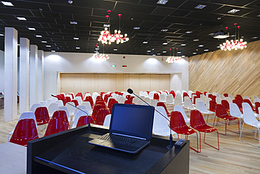 A laptop computer at a podium and rows of chairs in a large room