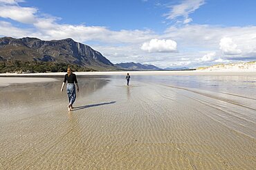 Teenage girl and her younger brother walking across a wide beach, Grotto Beach, Western Cape, South Africa