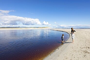 Teenage girl and a young boy at the edge of a wide water channel, on a sandy beach, Grotto Beach, Western Cape, South Africa