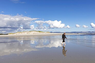 An adult man wearing a hat walking along a sandy beach, Grotto Beach, Western Cape, South Africa