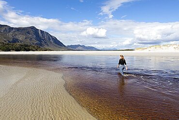 A teenage girl wading through a water channel on a wide sandy beach, Grotto Beach, Western Cape, South Africa