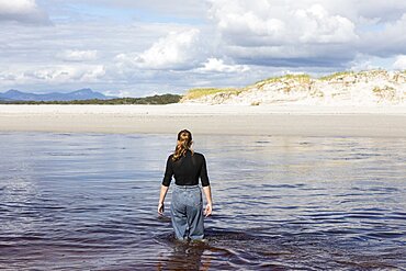 A teenage girl wading through a water channel on a wide sandy beach, Grotto Beach, Western Cape, South Africa