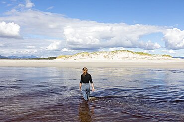 A teenage girl wading through a water channel on a wide sandy beach, Grotto Beach, Western Cape, South Africa