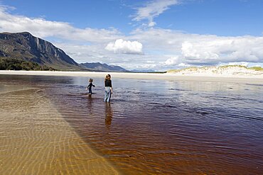 Teenage girl and young boy on an open sandy beach wading through shallow water, Grotto Beach, Western Cape, South Africa