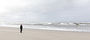 A man walking across sand to the water's edge on a beach, overcast day and surf waves breaking on shore, Grotto Beach, Western Cape, South Africa