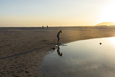 Boy on a beach, looking at his reflection in a water pool, low tide, sunset, Grotto Beach, Western Cape, South Africa