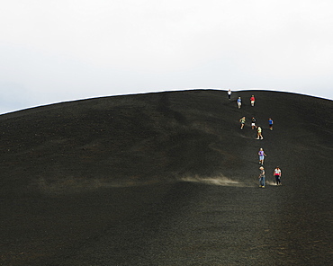 People walking through the lava fields and up a volcano slope of the Craters of the Moon National Monument.